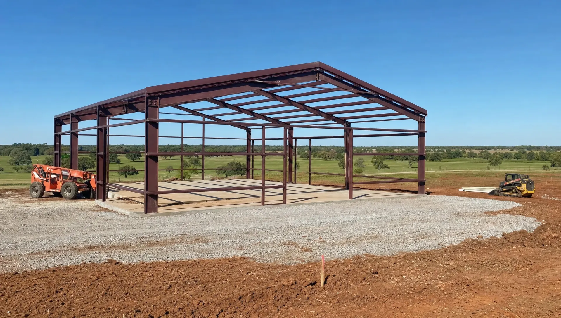 A custom metal building project on Oklahoma acreage with a framed structure, prepared foundation area, construction equipment, and open land in the background.