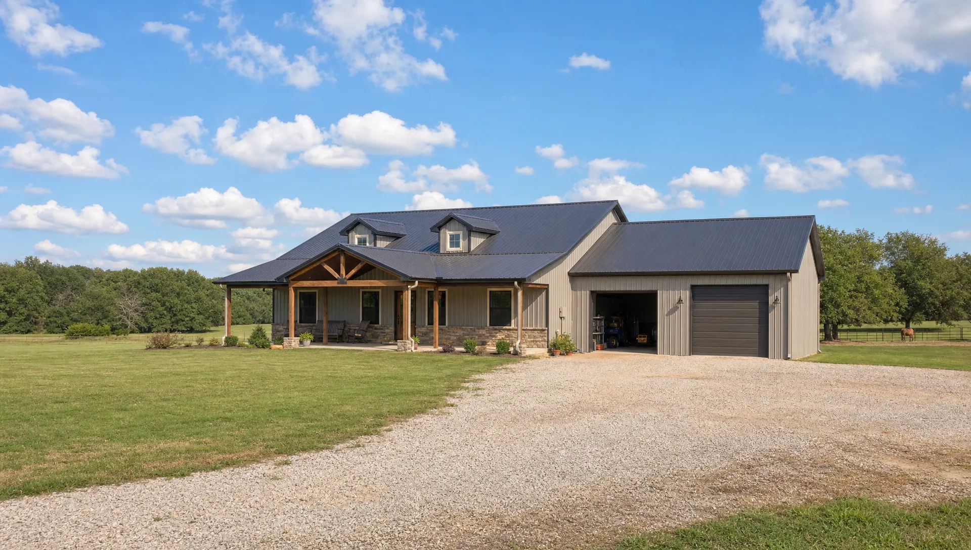 A rural Oklahoma homesite with a custom barndominium, attached shop space, covered porch, gravel drive, open pasture, and tree line in the distance under a wide sky.